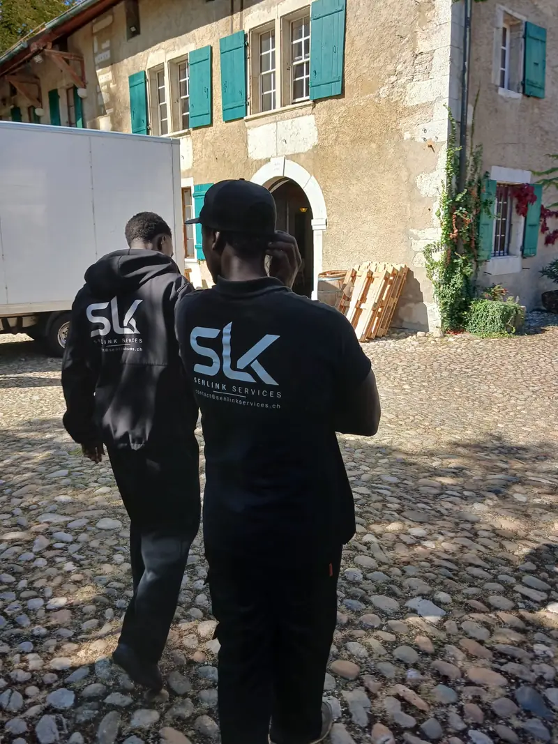 Deux employés SENLINK de dos, logos SLK visibles, dans une cour pavée