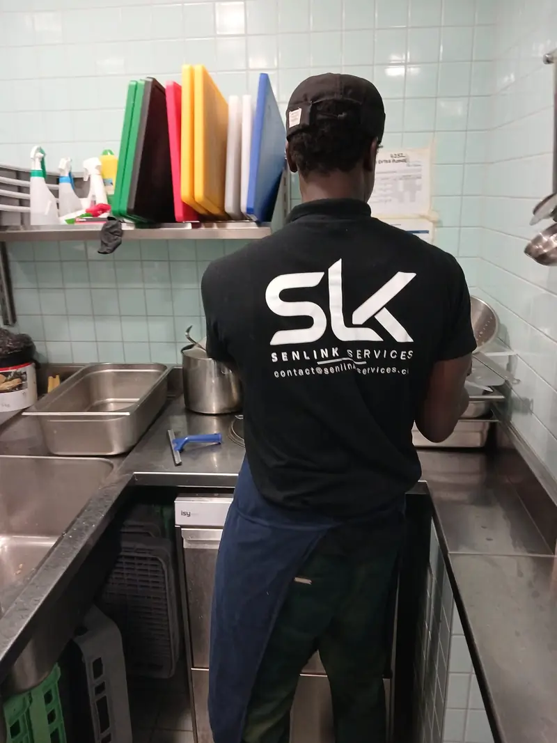 Plongeur SENLINK de dos, logo SLK sur le t-shirt, au poste de plonge